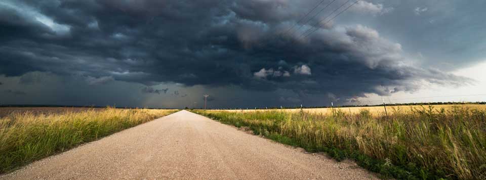 A dirt road with bad weather on the horizon