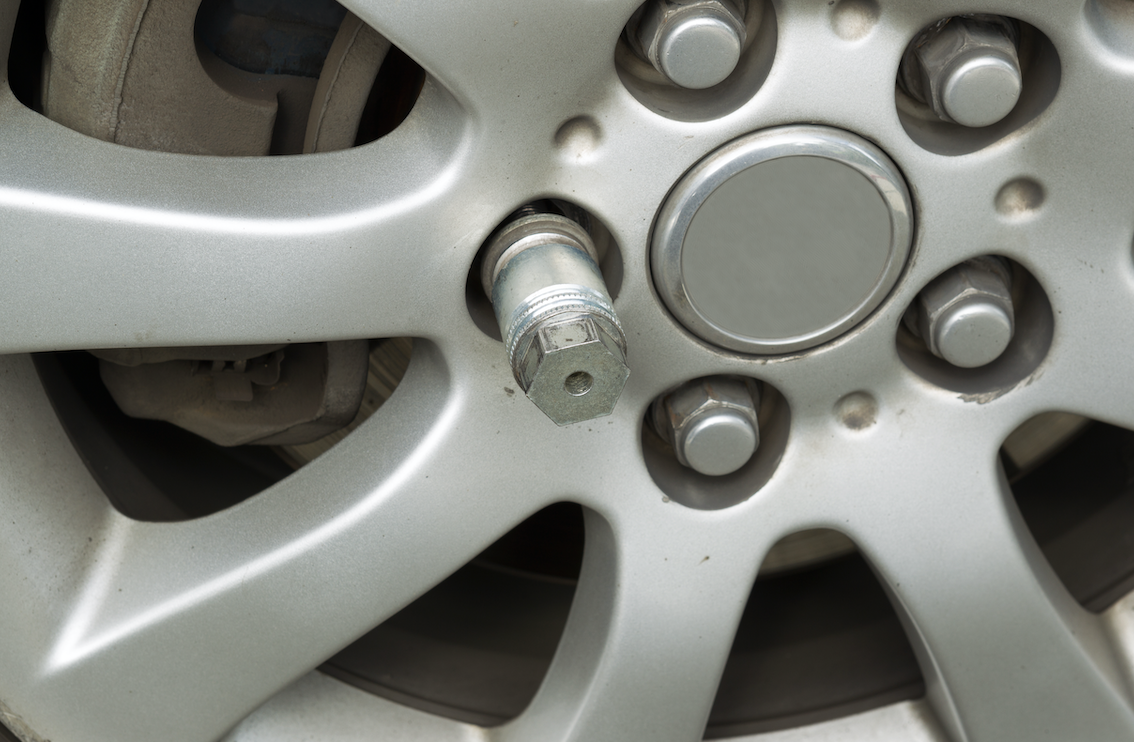 Red jumper cables coiled inside a spare tire well, showing emergency roadside equipment with black diamond-plate surface visible above.