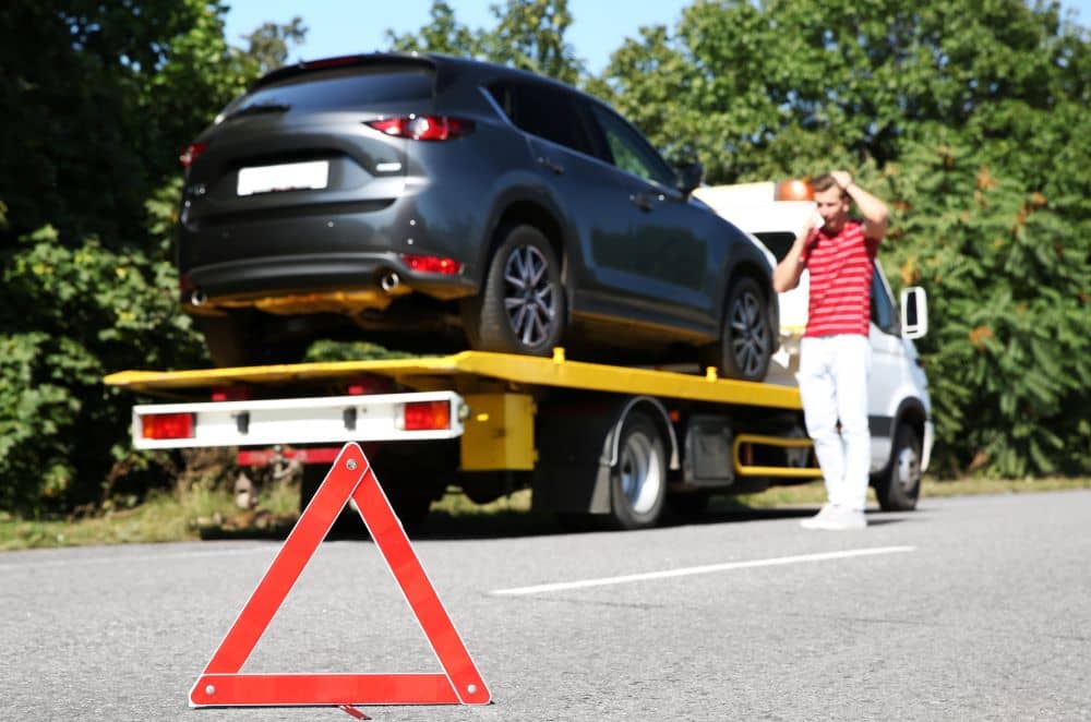 Man on the side of the road with his towed car.